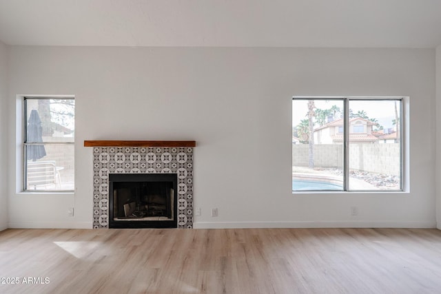 unfurnished living room featuring baseboards, a tiled fireplace, and wood finished floors