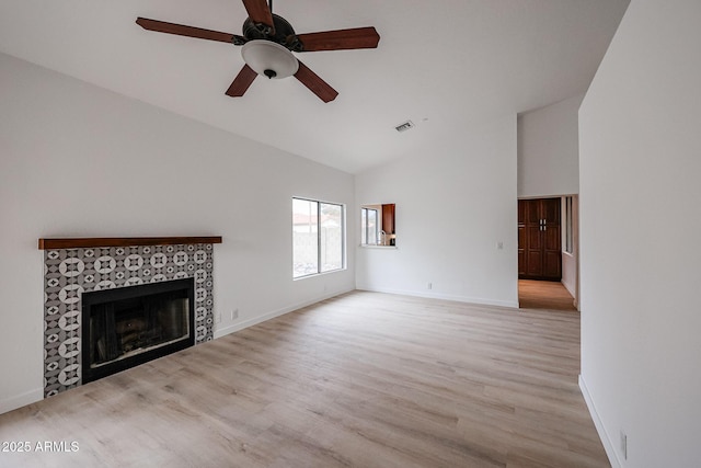 unfurnished living room featuring a tiled fireplace, ceiling fan, high vaulted ceiling, and light hardwood / wood-style flooring