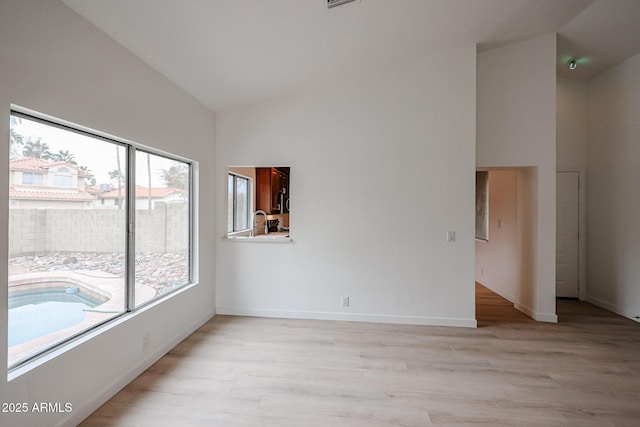 empty room with high vaulted ceiling, light wood-style flooring, and baseboards