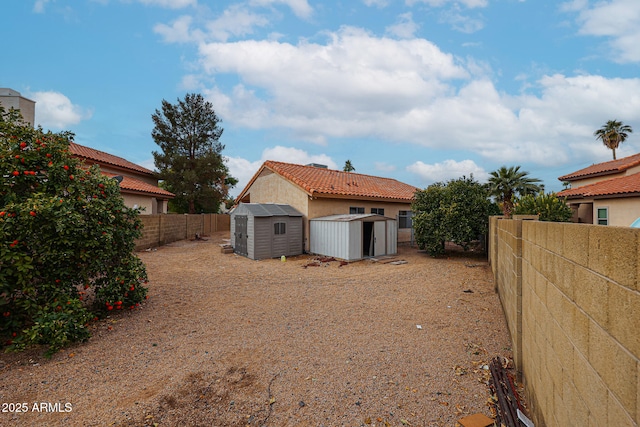 rear view of property with an outbuilding, a tile roof, stucco siding, a storage unit, and a fenced backyard