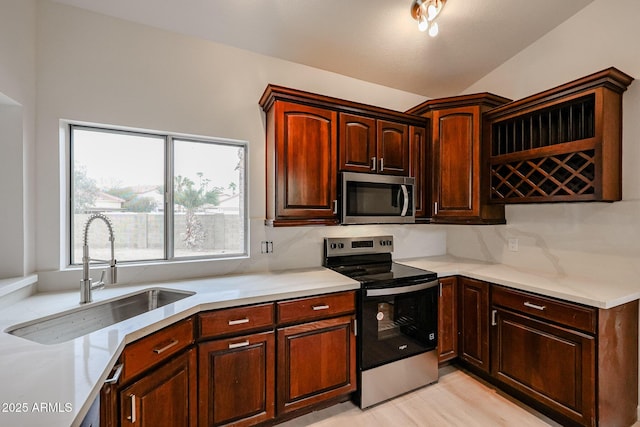 kitchen featuring lofted ceiling, appliances with stainless steel finishes, light countertops, light wood-type flooring, and a sink