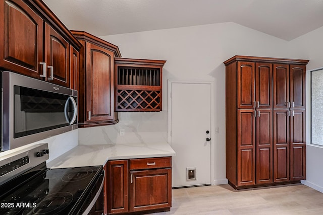 kitchen with lofted ceiling, light wood-type flooring, light stone countertops, and appliances with stainless steel finishes