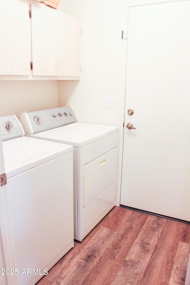 clothes washing area with cabinets, washer and dryer, and light hardwood / wood-style flooring