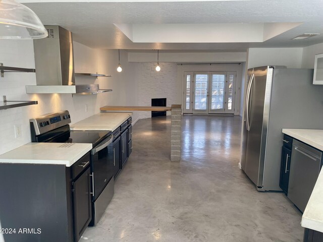 kitchen featuring hanging light fixtures, a brick fireplace, stainless steel appliances, wall chimney range hood, and a textured ceiling