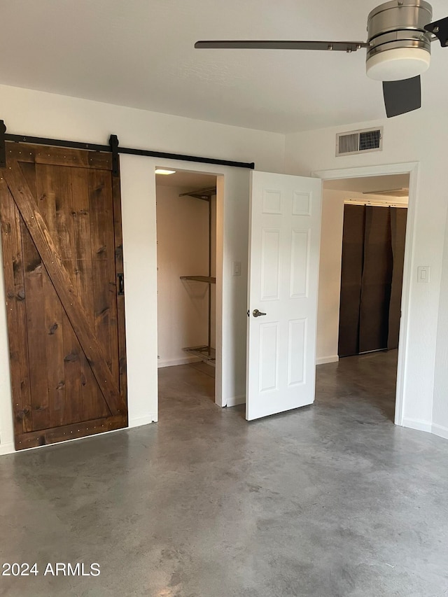 unfurnished bedroom with a barn door and ceiling fan