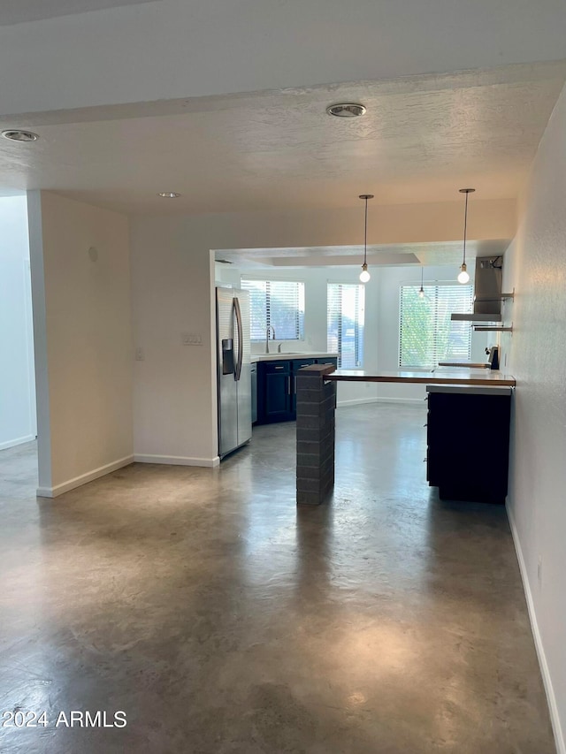 kitchen featuring pendant lighting, a kitchen bar, exhaust hood, sink, and stainless steel refrigerator with ice dispenser