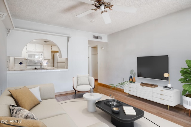 living room featuring ceiling fan, light hardwood / wood-style flooring, and a textured ceiling