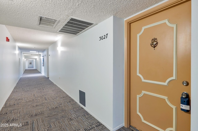 hall featuring dark carpet and a textured ceiling