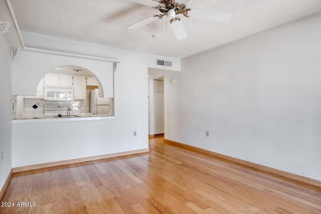 unfurnished living room featuring ceiling fan, a textured ceiling, and light wood-type flooring