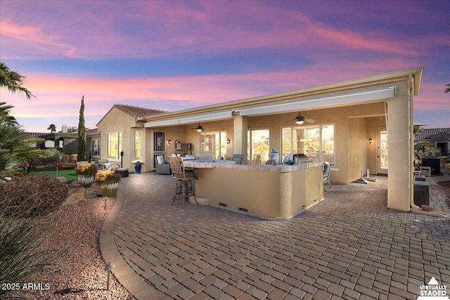 patio terrace at dusk featuring a bar and ceiling fan