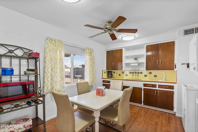 dining room featuring hardwood / wood-style floors, ceiling fan, sink, and brick wall