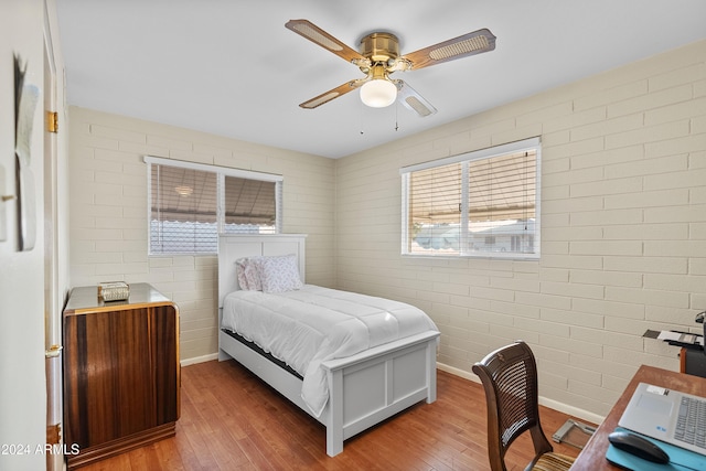 bedroom featuring hardwood / wood-style flooring, ceiling fan, and brick wall