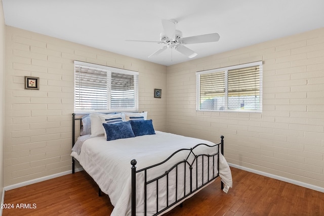 bedroom with ceiling fan, dark wood-type flooring, and brick wall