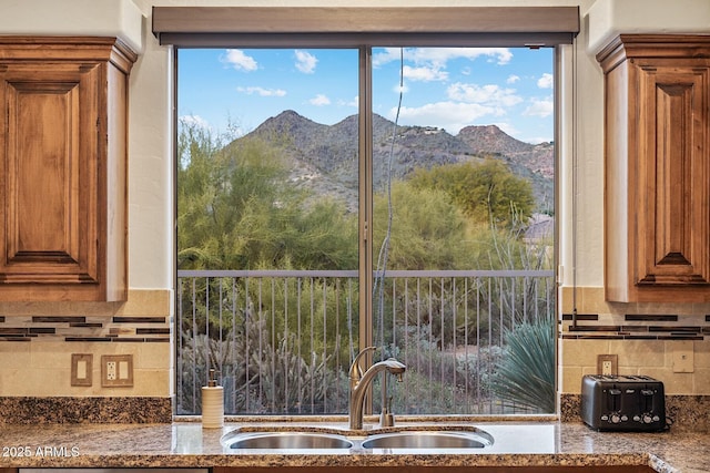 kitchen with tasteful backsplash, stone countertops, brown cabinetry, a mountain view, and a sink