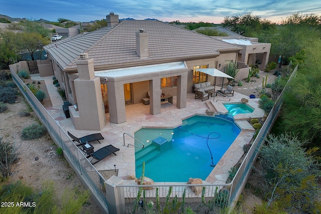 rear view of property featuring stucco siding, a pool with connected hot tub, a patio area, a fenced backyard, and a tiled roof