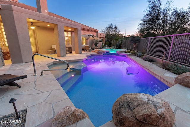 pool at dusk featuring a patio area, fence, and a pool with connected hot tub