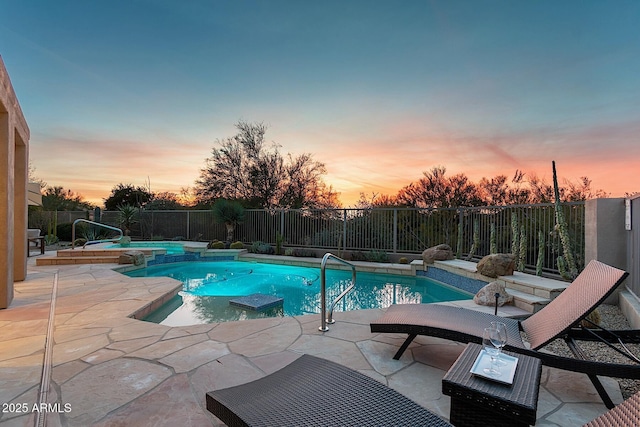 pool at dusk featuring a fenced backyard, a pool with connected hot tub, and a patio