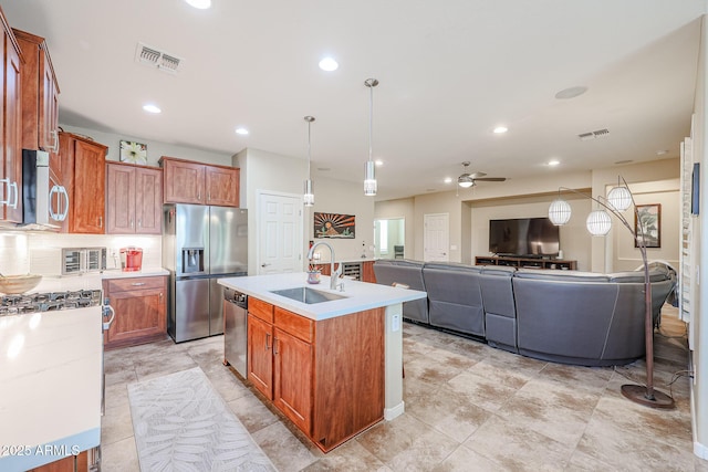 kitchen featuring a center island with sink, sink, stainless steel appliances, hanging light fixtures, and tasteful backsplash