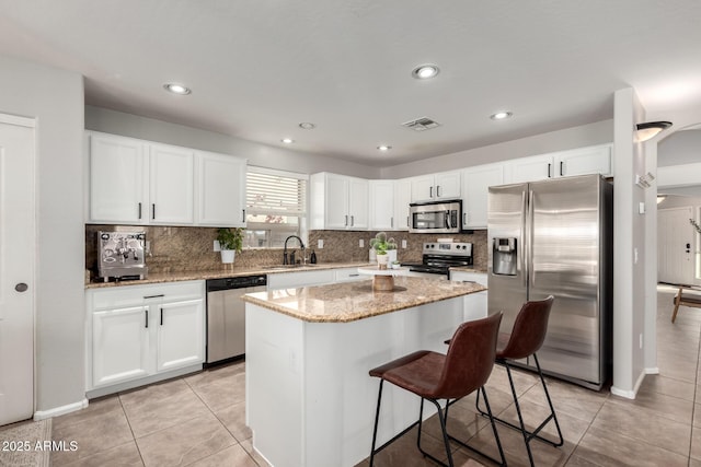 kitchen featuring appliances with stainless steel finishes, white cabinetry, a center island, light stone counters, and light tile patterned flooring