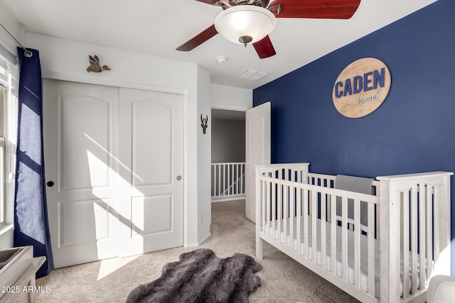 bedroom with ceiling fan, light colored carpet, a closet, and a crib