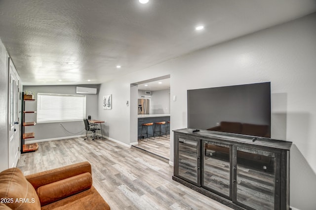 living room featuring a wall mounted air conditioner, light hardwood / wood-style floors, and a textured ceiling