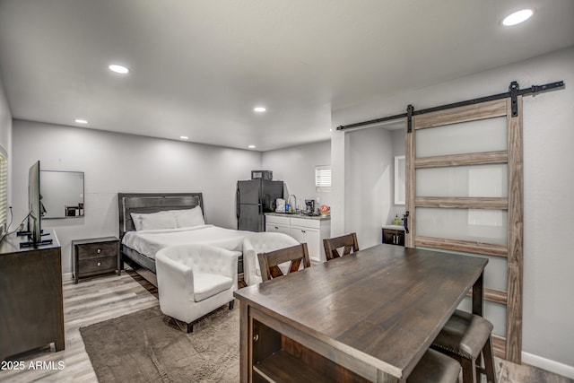 bedroom with light wood-type flooring, a barn door, and black fridge