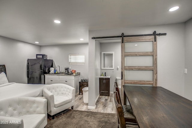 bedroom featuring a barn door, black refrigerator, sink, and light hardwood / wood-style floors