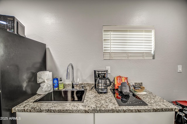 kitchen featuring black refrigerator, light stone countertops, and sink