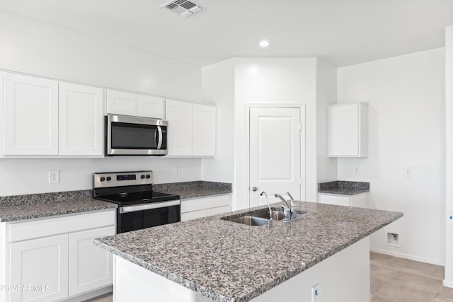 kitchen with appliances with stainless steel finishes, white cabinetry, sink, dark stone counters, and a kitchen island with sink