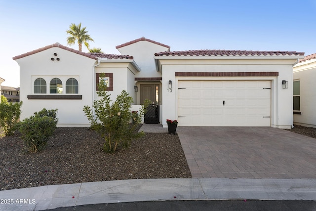 mediterranean / spanish-style house with a garage, a tiled roof, decorative driveway, and stucco siding