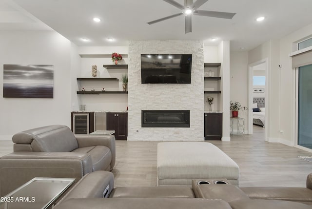 living area featuring wine cooler, a stone fireplace, light wood-style floors, built in shelves, and recessed lighting