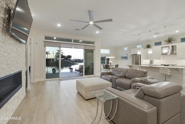 living area with a fireplace, recessed lighting, a water view, light wood-style floors, and ceiling fan