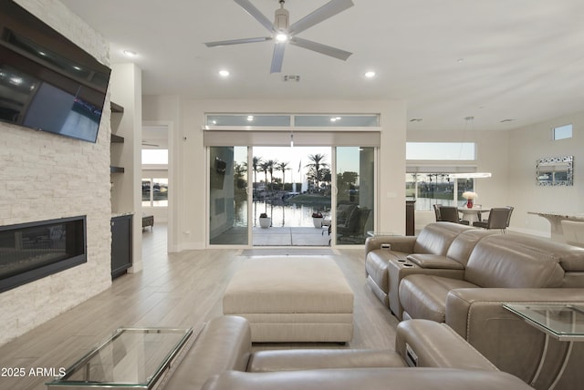 living room featuring light wood-type flooring, ceiling fan, a fireplace, and recessed lighting