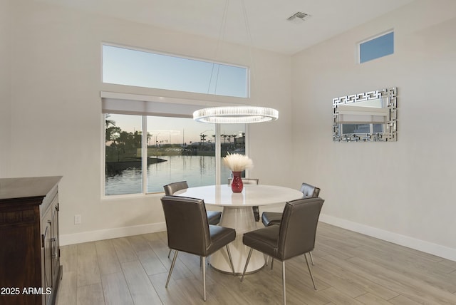 dining area with light wood-type flooring, a water view, visible vents, and baseboards