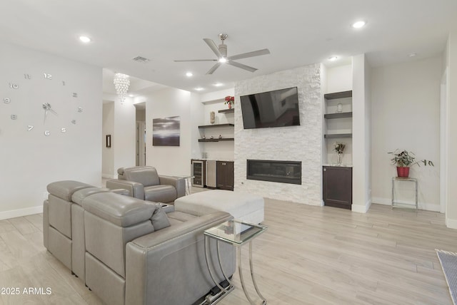 living area featuring built in features, visible vents, a stone fireplace, and light wood finished floors