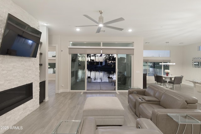 living area with baseboards, a ceiling fan, light wood-style flooring, a stone fireplace, and recessed lighting