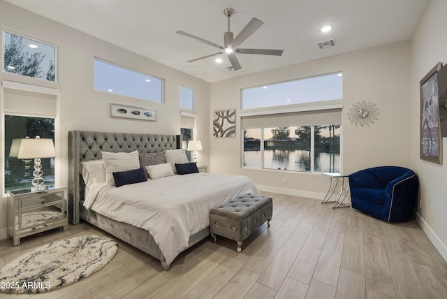 bedroom featuring ceiling fan, a water view, visible vents, baseboards, and light wood-style floors