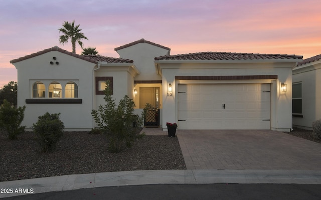 mediterranean / spanish-style house with a garage, decorative driveway, a tile roof, and stucco siding