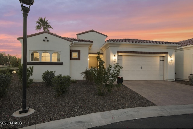 mediterranean / spanish-style house with a garage, decorative driveway, a tiled roof, and stucco siding