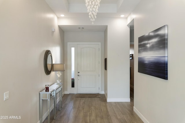 doorway to outside featuring recessed lighting, wood finished floors, visible vents, baseboards, and a tray ceiling