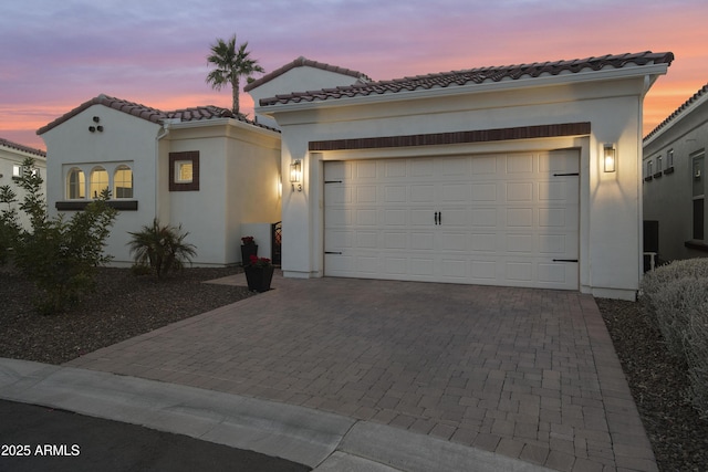 mediterranean / spanish-style home with decorative driveway, a tiled roof, an attached garage, and stucco siding