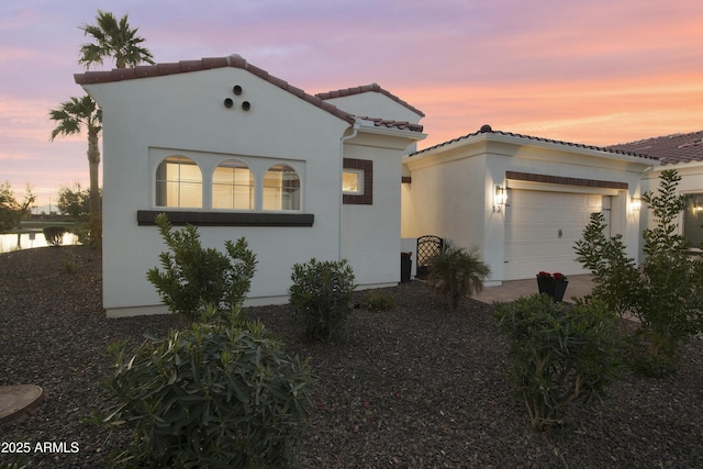 mediterranean / spanish-style house with a garage, a tiled roof, and stucco siding