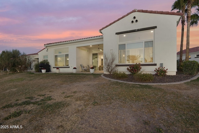 back of house at dusk featuring a lawn, a tile roof, and stucco siding