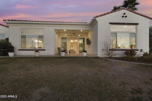 back of property with a yard, stucco siding, a patio area, ceiling fan, and a tiled roof