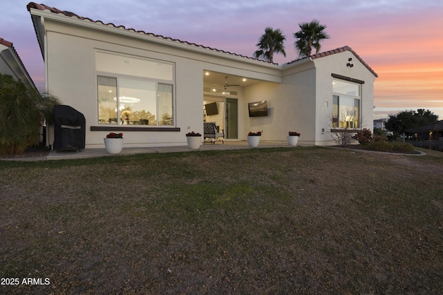 back of property featuring stucco siding, a tiled roof, a patio, and a yard