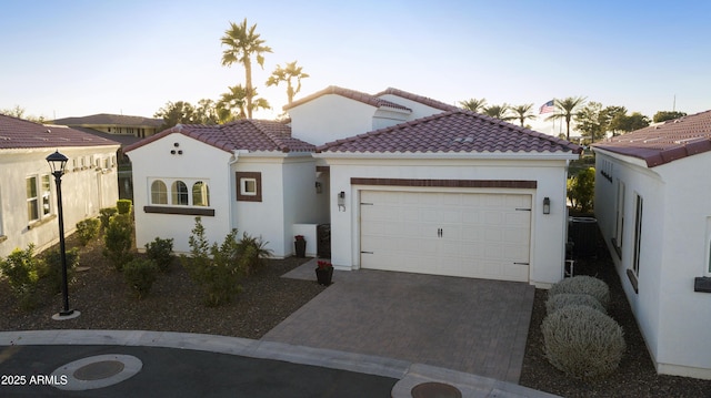 mediterranean / spanish home featuring a garage, a tile roof, decorative driveway, and stucco siding