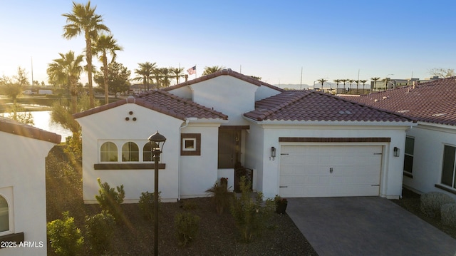 mediterranean / spanish house featuring driveway, a garage, a tiled roof, a water view, and stucco siding