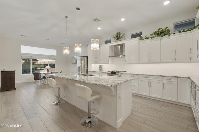 kitchen featuring white cabinetry, a center island with sink, decorative light fixtures, and wall chimney exhaust hood