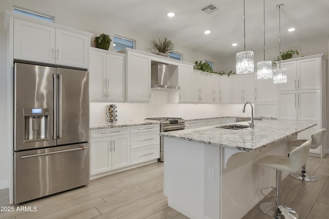 kitchen with visible vents, appliances with stainless steel finishes, a kitchen island with sink, white cabinets, and wall chimney exhaust hood