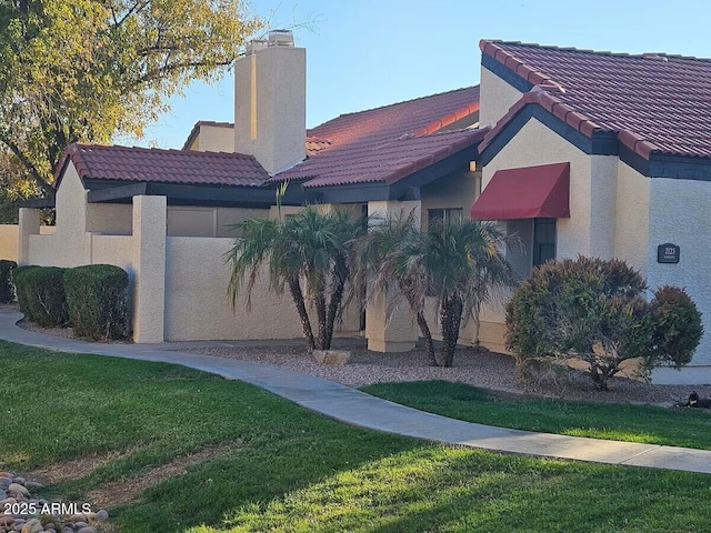 view of front of house with a tiled roof, stucco siding, a front lawn, and a chimney